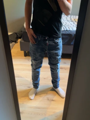 Blå slitna skinny jeans herr - Säljer ett par blå skinny jeans med slitningar och hål på benen samt små färgstänk för en trendig look. Jeansen har fem fickor och knappgylf. Perfekta för dig som gillar streetwear och vill ha en avslappnad men snygg stil.