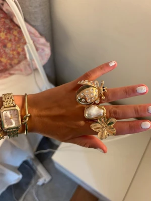 Guld ringar och armband  - Säljer tre unika statementringar i guldton. En ring har en stor nyckelpiga dekorerad med klara stenar, en har en oregelbunden pärlliknande sten och den tredje är formad som ett fyrklöver. Perfekta för dig som vill sticka ut och addera något extra till din stil. Skit snygga unika smycken. Säljer var för sig eller tillsammans så skriv vilket smycke du är intresserad av så ger jag pris osv