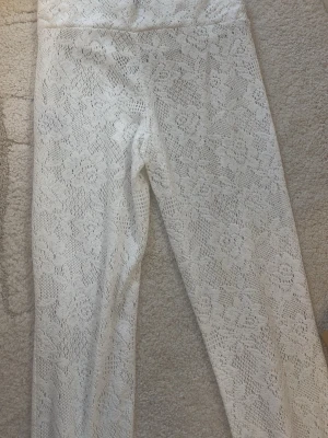 Vita spetsleggings med blommönster - Säljer ett par vita leggings med snyggt blommigt spetsmönster. De är stretchiga vilket gör dem bekväma och stilrena. Perfekta för dig som vill ha en unik och trendig look med lite extra detaljer.