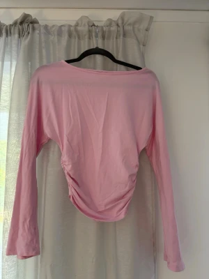 Ljusrosa långärmad top från Gina - Söt ljusrosa långärmad topp med rynkade detaljer i sidan som ger en snygg form. Tillverkad i mjukt bomullstyg och har en enkel, stilren design med rund halsringning. Storlek 158/164 men skulle säga att den passar xxs/xs också