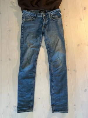 Blå slim fit jeans från Replay - Snygga blå slim fit jeans från Replay med klassisk femficksdesign och dragkedjegylf. Jeansen har en tvättad look med lätt slitningar och smal passform som sitter tajt längs benen. Perfekta för en trendig och avslappnad stil. W 28 L 30