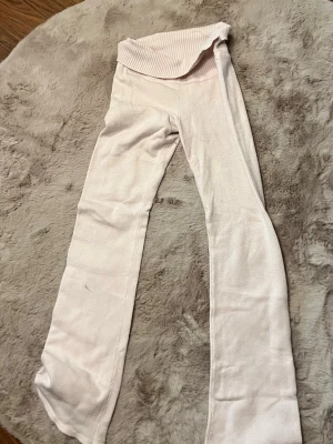 Ljusrosa ribbade leggings med utsvängda ben - Supersnygga ljusrosa leggings med ribbad, hög midja och utsvängda ben. Mjukt och stretchigt material som sitter bekvämt och följer kroppen. Perfekta för en trendig och avslappnad look.