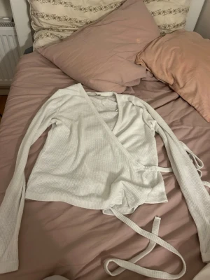 Vit omlottopp och skjorta - Säljer en vit ribbad omlottopp med långa ärmar och knytband i midjan samt en vit skjorta med knappar och bröstfickor. Perfekta basplagg att styla till olika looks.
