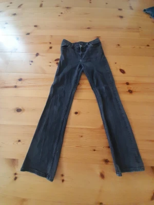 Blå bootcut jeans med fickdetaljer - Snygga blå bootcut jeans med klassiska fem fickor och dekorativa sömmar på bakfickorna. Jeansen har låg midja och utsvängda ben, perfekta för en retroinspirerad look. Tillverkade i denim med kontrastsömmar.