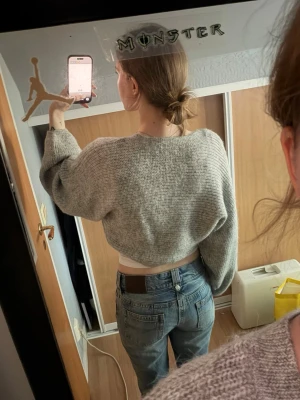 Grå stickad bolero  - Säljer en grå, stickad bolero med breda ärmar och avslappnad passform. Tröjan har en enkel, klassisk stickning och är perfekt att slänga över ett linne eller t-shirt. Materialet ser mjukt och mysigt ut, perfekt för lager på lager. Djur finns i hemmet! 