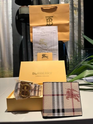 Rutigt bälte med guld spänne - Snyggt bälte med klassiskt rutigt mönster i beige, svart, vitt och rött. Bältet har ett stort guldigt spänne med den ikoniska loggan. Perfekt accessoar för att lyfta din outfit. En plånbok också. Hör av er vid fler frågor😁