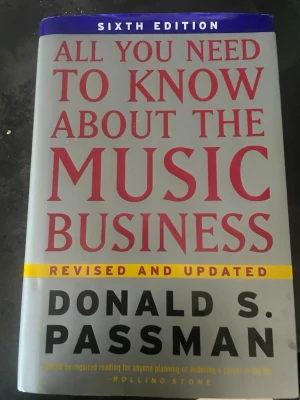 All You Need to Know About the Music Business - Sjätte upplagan av 'All You Need to Know About the Music Business' av Donald S. Passman. Boken har ett grått omslag med stora röda och svarta bokstäver samt en gul markering för 'Revised and Updated'. Perfekt för dig som vill förstå musikbranschen.
