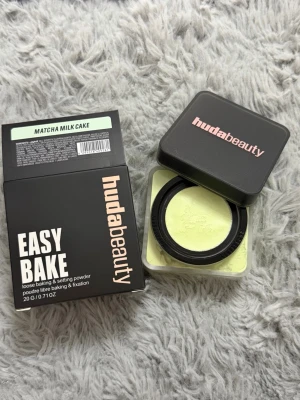 Huda Beauty Easy Bake Matcha Milk Cake - Lös baking- och settingpuder från Huda Beauty i färgen Matcha Milk Cake. Pudret har en ljusgrön ton och kommer i en fyrkantig plastburk med svart lock. Perfekt för att fixera basen och ge en matt finish.