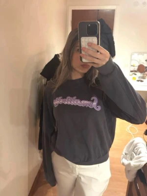 Mörkgrå sweatshirt med lila text - Mörkgrå sweatshirt med lila texttryck framtill. Den har en liten fläck.💕