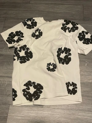 Vit t-shirt med svarta blommor - Säljer en vit t-shirt står ingen storlek i tröjan men skulle själv säga att de är en S men mått kan skickas privat 