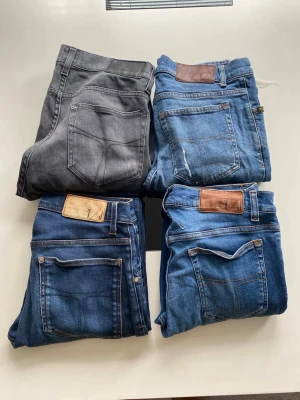 Fyra par jeans i olika blå nyanser - Säljer fyra par jeans i olika blå tvättar och ett par i grått. Alla har klassisk femficksdesign, raka eller smala ben och detaljer i brunt läder vid linningen. Perfekta för dig som gillar en avslappnad men stilren look.