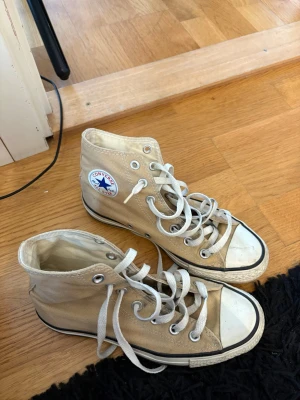 Beige Converse Chuck Taylor Highs - Säljer ett par beige Converse Chuck Taylor All Star high tops med vita gummisulor och tåhättor. Klassisk logga på sidan. Lite smutsiga se bild 