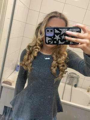 Mörkgrå ribbstickad peplumtröja - Mysig mörkgrå stickad tröja med ribbad struktur och peplumformad midja. Tröjan har långa ärmar och en något bredare rund halsringning. Perfekt för dig som gillar en feminin siluett och vill ha något både bekvämt och snyggt.