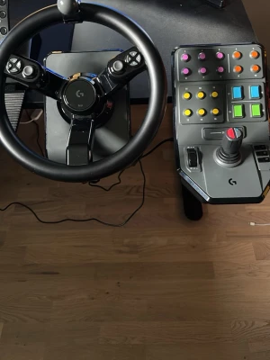 Logitech ratt, pedaler och kontrollpanel - Säljer ett komplett Farming simulator kit från Logitech med ratt, pedaler och avancerad kontrollpanel. Ratten är svart med spakar och har flera knappar. Kontrollpanelen har färgglada knappar och joystick, perfekt för simulatorer. Pedalerna är robusta och svarta.