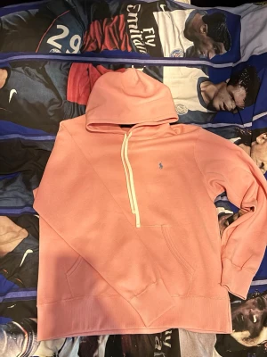 Ljusrosa Ralph Lauren hoodie - Säljer en ljusrosa hoodie med huva från Ralph Lauren. Hoodien har en liten blå logga broderad på bröstet och en stor magficka. Tillverkad i mjukt bomullsmaterial, perfekt för att få en liten extra snygg look. Det är storlek L men passar även M. Priset går alltid att diskutera!