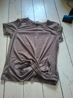 Beige t-shirt med twistad detalj - Säljer en beige t-shirt i mjuk bomull med korta ärmar och rund hals. Framtill har den en twistad detalj som ger en snygg och avslappnad look. Perfekt till jeans eller kjol för en enkel men trendig stil.