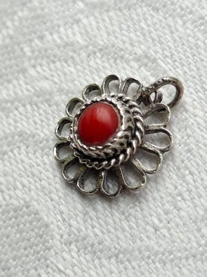 Retro etno silverberlock med röd korall - Söt berlock för retro/etno/bohoentusiaster kanske. Smycket inköptes i Turkiet kring 1960 av min mormor som var mycket kunnig i utländskt guld och silver. Det är gjort i ett enklare filigranarbete och bär de naturliga spåren av handgjort. Troligtvis har det jemenitiskt ursprung. Gott skick. Bredd 12 mm.