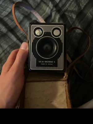 Kodak Six-20 Brownie E boxkamera - Säljer en klassisk Kodak Six-20 'Brownie' E boxkamera i svart metall med vita detaljer. Kameran har en retro design och levereras med ett brunt fodral i läder med axelrem. Perfekt för dig som gillar vintagekameror och analog fotografering. Kameran är Otestad 