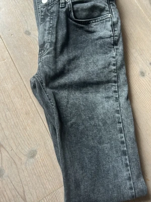 Grå tvättade bootcut jeans - Snygga grå jeans med tvättad look och bootcut. Klassisk femficksmodell med knapp och dragkedja framtill. Jeansen har en avslappnad passform och passar perfekt till en trendig outfits.passar till mycket. 