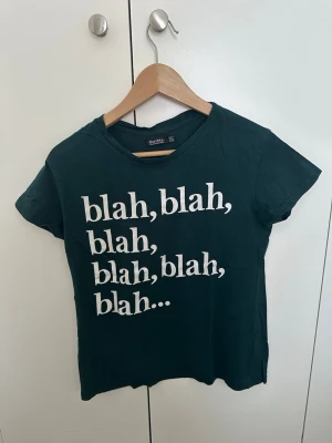 Mörkgrön t-shirt från Bershka - Mörkgrön t-shirt från Bershka med vit text 'blah, blah, blah...' på framsidan. Klassisk rund hals och korta ärmar. Tillverkad i mjuk bomull som känns skön mot huden. Perfekt för dig som gillar statement-plagg med attityd.