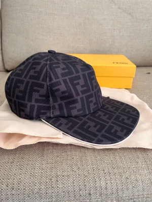 Fendi keps - Snygg svart keps från Fendi med det klassiska FF-monogrammet över hela kepsen. Kepsen har böjd skärm och justerbar rem bak. Tillverkad i ett slitstarkt tyg som ger en exklusiv känsla. Perfekt för dig som vill ha en trendig accessoar med lyxig touch.