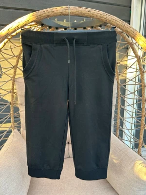 Mjukiscapri till pojkar - Säljer ett par svarta mjukisbyxor med ribbad midja och dragsko. Byxorna har två sidofickor och muddar vid bensluten för en skön och avslappnad look. 