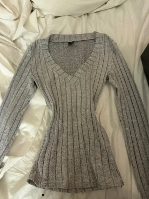 Grå ribbstickad tröja från SHEIN - Snygg grå ribbstickad tröja från SHEIN med figurnära passform och djup V-ringning. Långa ärmar och vertikala ränder ger en trendig look. Perfekt att matcha med jeans eller kjol för en stilren outfit. Också sydd av mig på midjan för en smalare look i midjan.