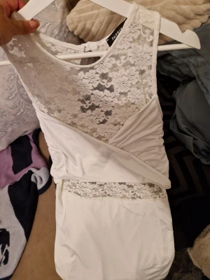 Vit spetsklänning med omlott - Snygg vit kortklänning med spets upptill och omlottdetalj framtill. Klänningen har ärmlös design och blommigt spetsmönster som ger en romantisk vibe. Perfekt för sommarens alla tillfällen! Den sitter skit snyggt på!! Passar s/m 