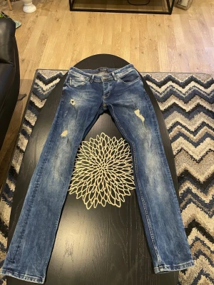 Armani jeans  - Säljer ett par blå armani jeans med slitningar och tvättade detaljer. Jeansen har klassisk femficksmodell, låg midja och dragkedja. Perfekta för en avslappnad och trendig look.