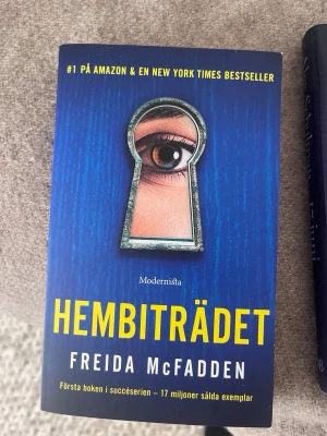 Hembiträdet av Freida McFadden - Spännande roman med blått omslag och ett öga som kikar genom ett nyckelhål. Boken är skriven av Freida McFadden och utgiven av Modernista. Perfekt för dig som gillar thrillers och mysterier.