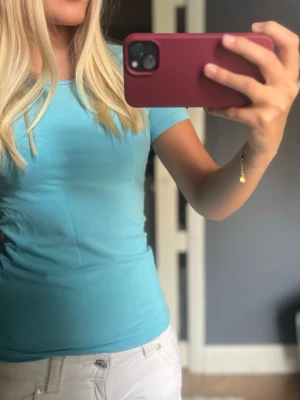 Ljusblå/turkos tight t-shirt - Snygg ljusblå t-shirt med korta ärmar och rund halsringning. Modellen är tight och passar perfekt till jeans eller shorts. Enkel och stilren design utan tryck eller mönster. den har en liten fläck men syns knappt