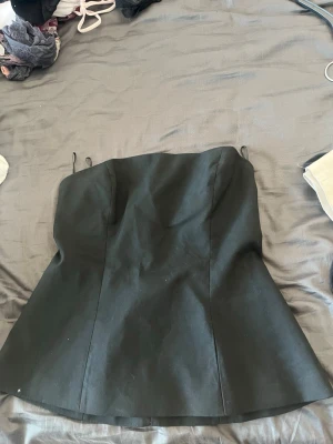 Svart axelbandslös korsettopp - Snygg svart korsettopp med axelbandslös design och figurnära passform. Toppen har en enkel och stilren look som passar perfekt till många olika outfits. Materialet känns stadigt och ger en smickrande siluett.