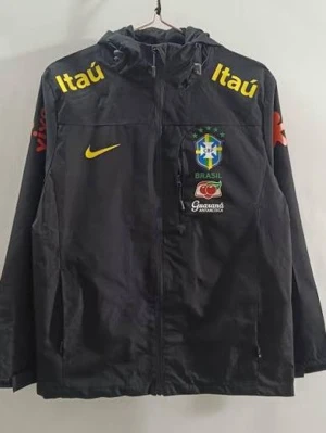 Svart Brasilien Nike vindjacka - Svart vindjacka med huva från Nike, prydd med Brasilien fotbollslandslagets logga och flera sponsorloggor i gult, vitt och rött. Jackan har dragkedja framtill, fickor och justerbar huva. Perfekt för dig som gillar sportig stil och vill sticka ut. den är xl men passar för m och l.Mer bilder kommer snart för jag är på semester nu .