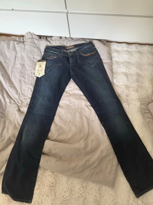 Vintage Jeans - Säljer ett par mörkblå, lätt bootcut jeans med snygga kontrastsömmar och dekorativa bakfickor. Jeansen har klassisk femficksmodell och är tillverkade i denim med lätt tvättad look. Perfekta för dig som gillar en tidlös och avslappnad stil. De är i storlek 28 vilket motsvarar ungefär 36.De är helt oanvända och priset går att diskutera!! 