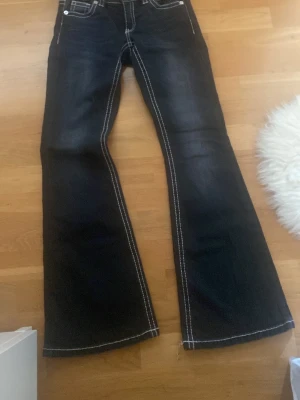 Svarta bootcut jeans med kontrastsömmar - Säljer ett par mörkblå bootcut jeans med vita kontrastsömmar och broderade bakfickor. Jeansen har klassisk femficksmodell och utsvängda ben. Perfekta för dig som gillar retrovibbar och vill sticka ut lite extra.