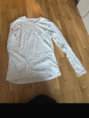 Vit långärmad topp i bomull - En enkel och stilren vit långärmad topp i mjuk bomull. Perfekt basplagg med rund halsringning och normal passform. Passar till allt och är superenkel att styla med andra plagg.