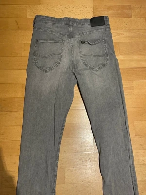 Grå raka jeans från Lee - Säljer ett par grå jeans från Lee med klassisk femficksmodell och raka ben. Jeansen har en diskret tvättad look och Lee-logga på bakre linningen. Perfekta för en avslappnad och stilren outfit.