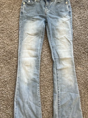 Ljusblå bootcut jeans - Säljer ett par ljusblå bootcut jeans med slitningar framtill och klassiska bakfickor med dekorsömmar. Jeansen har en något utsvängd passform nedtill och är tillverkade i denim. Perfekta för en avslappnad och trendig look.