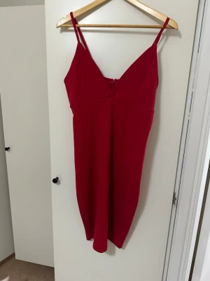 Röd klänning från BikBok med smala band - Snygg röd klänning från BikBok med smala axelband och v-ringning. Klänningen är kort och har en enkel, stilren design som passar perfekt när du vill sticka ut. Materialet känns lätt och bekvämt mot huden.