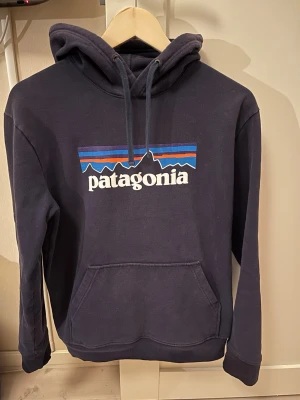 Mörkblå Patagonia hoodie - Snygg mörkblå hoodie från Patagonia med klassisk logga, storlek small regular fit, i använt skick men fortfarande i bra skick 