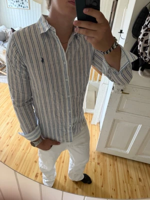 Randig skjorta i bomull - Säljer en vit linneskjorta från ralph lauren med blå ränder, den är i storlek XL men sitter mer som en vanlig L, den är i jättebra skick utan defekter