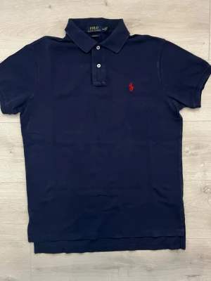 Ralph lauren pike  - Säljer en stilren mörkblå piké från Ralph Lauren. En klassisk och tidlös modell som passar lika bra till vardags som på sommaren eller vid lite finare tillfällen.  • Storlek: M • Färg: Mörkblå • Skick: Mycket fint skick • Broderad Ralph Lauren-logga på bröstet • Mjuk och bekväm passform • Perfekt att matcha med jeans, chinos eller shorts • Ett stilrent basplagg som aldrig går ur mode  En riktigt snygg piké i mycket fint skick. Hör av dig vid frågor eller om du vill ha fler bilder! 
