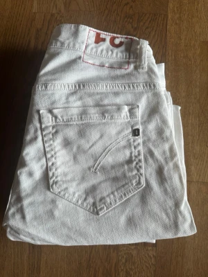 Vita raka jeans med röd detalj - Snygga vita jeans ifrån dondup passform George. Skick 10/10. Passar perfekt till en avslappnad och trendig stil. Hör av er vid minsta funderingar!