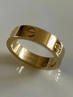Guldfärgad ring  - Snygg guldfärgad ring med klassisk skruvdetalj runt hela ringen. Ringen har en slät, blank yta och är tillverkad i metall. Perfekt för dig som gillar stilrena och ikoniska accessoarer.