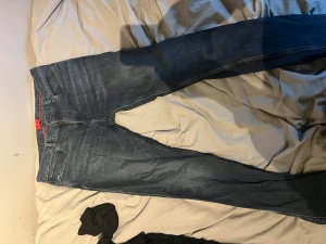 Mörkblå boss jeans - Snygga mörkblå jeans med klassisk femficksdesign och röda detaljer vid linningen. Jeansen har en något tvättad look och raka ben. Perfekta för en trendig och avslappnad stil. Sitter bra skriv vid frågor !