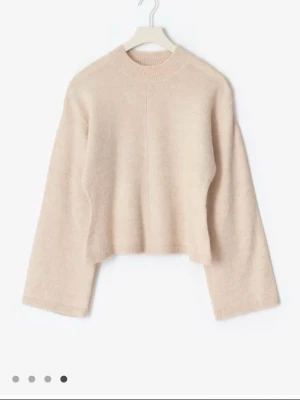 Gina tricot Beige stickad kofta med vida ärmar - Mysig beige stickad kofta  med rund hals och vida ärmar. Koftan har en rak, något kortare passform och ribbstickad kant vid halsen. Perfekt för lager på lager och enkel att matcha med jeans eller kjol.