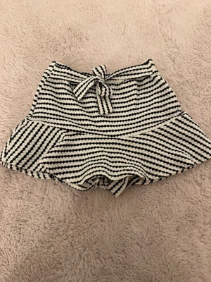 Kjol  - Säljer en svartvit randig kjol som har shorts undertill och ett knytband i midjan. Kjolen har en mjuk struktur och är perfekt för varma dagar. Den är tillverkade i ett bekvämt material som känns skönt mot huden.