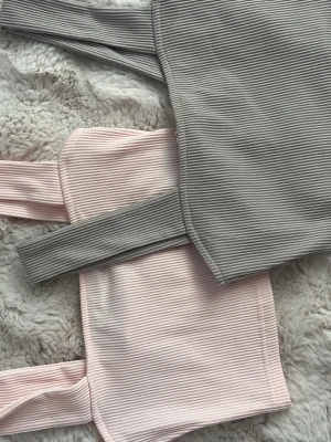 Ribbad crop top i grått och ljusrosa - Två ribbade crop tops med breda axelband, en i ljusgrått och en i ljusrosa. Toppens material är mjukt och stretchigt, perfekt för en chill och trendig look. Passformen är tight och modellen är ärmlös, vilket gör dem superenkla att styla.