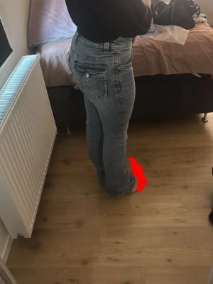 Grå bootcut jeans med tvättad look - Säljer ett par grå bootcut jeans med snygg tvättad effekt och klassiska fem fickor. Jeansen har låg midja och raka ben som slutar i en lätt utsvängd form. Perfekta för en avslappnad och trendig stil.