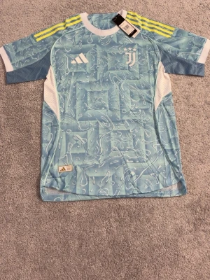 Juventus matchtröja blå Adidas - Snygg Juventus matchtröja i ljusblått med vitt och gula detaljer. Tröjan har korta ärmar, tryckt Juventus-logga och Adidas-märke på bröstet samt nummer 10 och Yildiz på ryggen. Tillverkad i lätt och ventilerande funktionsmaterial.